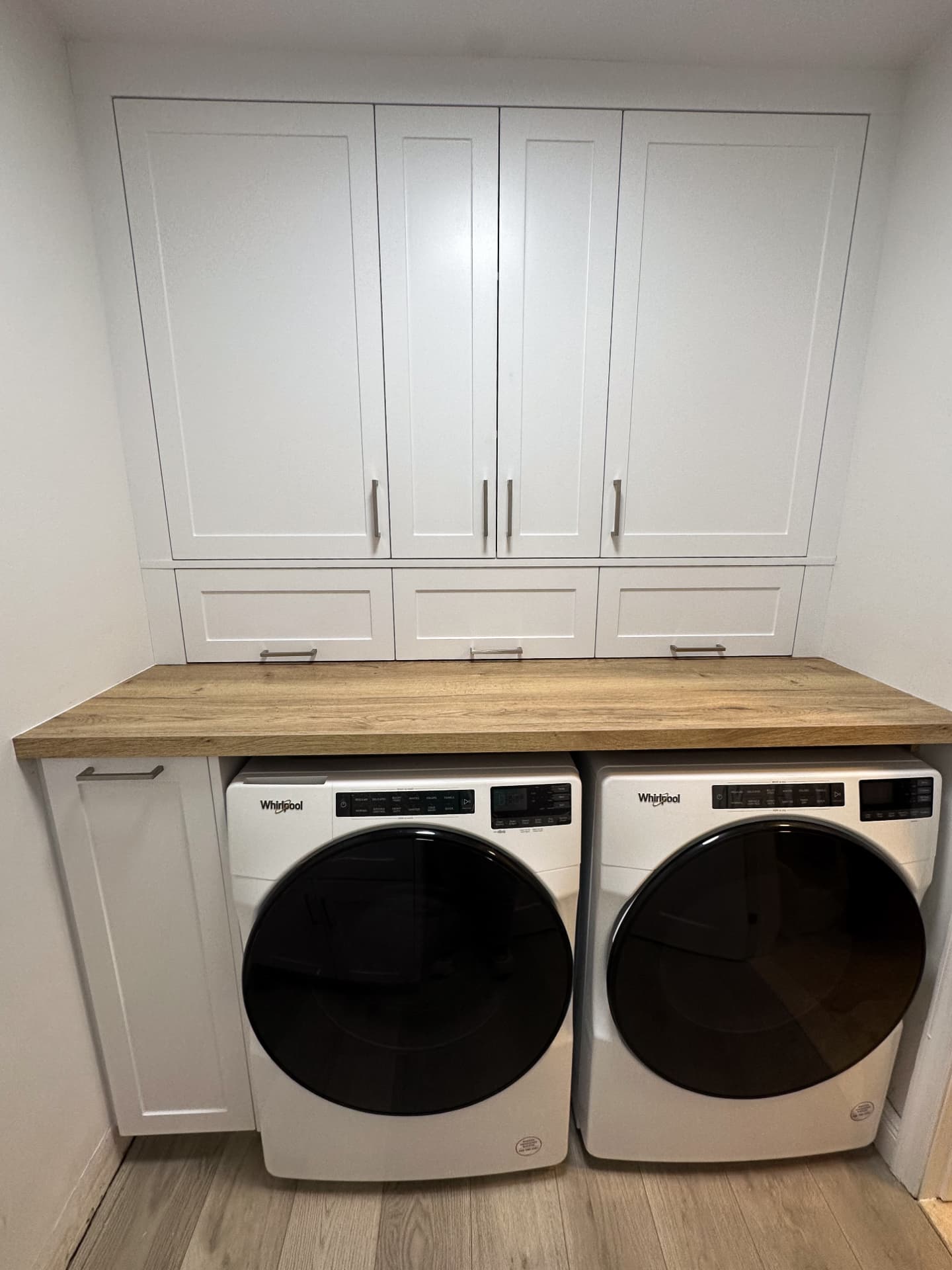 White laundry room cabinets with wood counter above washer and dryer