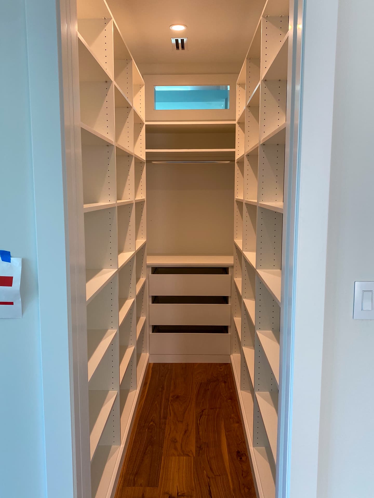 Narrow walk-in closet lined with white shelving