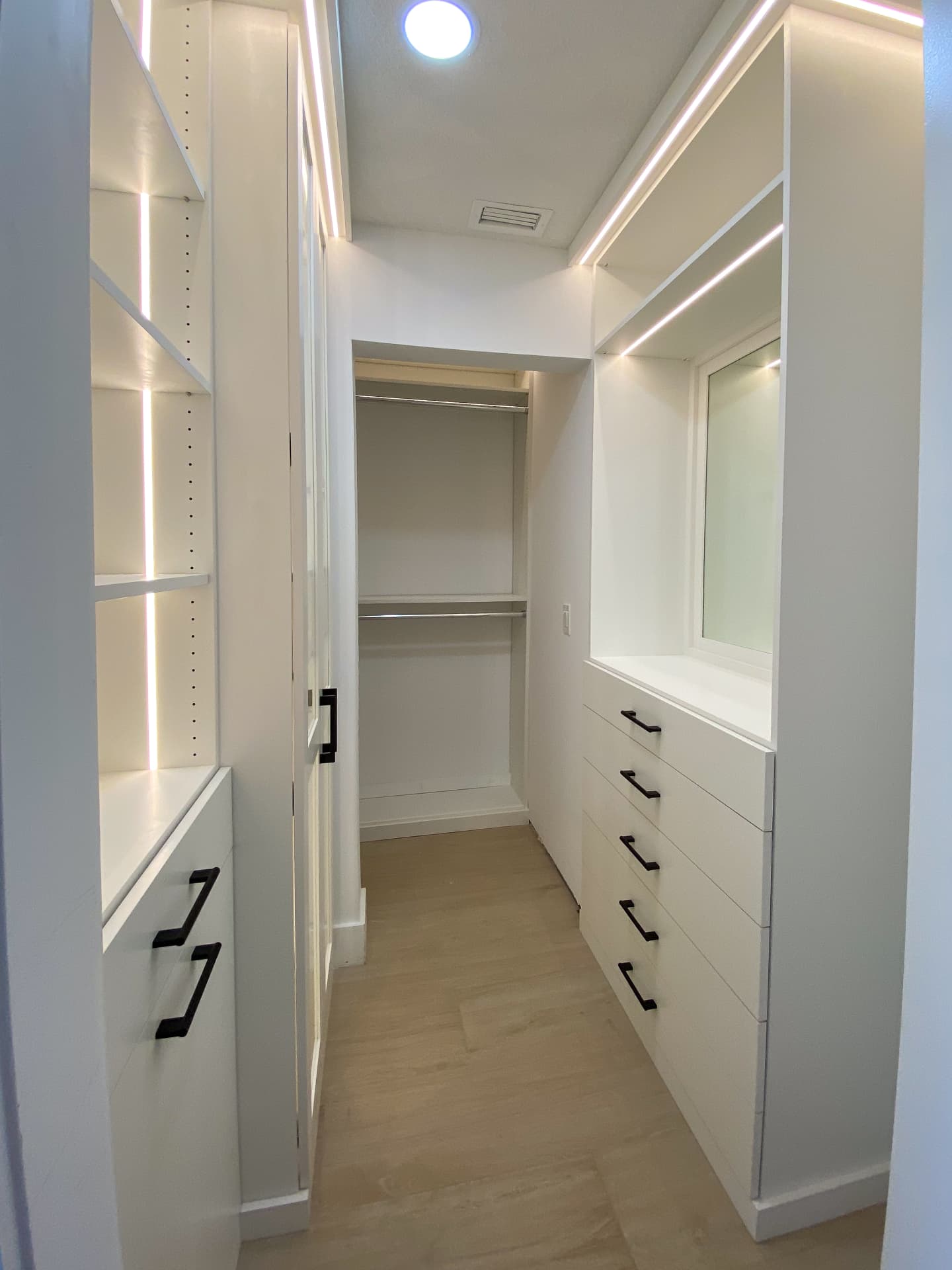 Long white walk-in closet with lit glass shelving